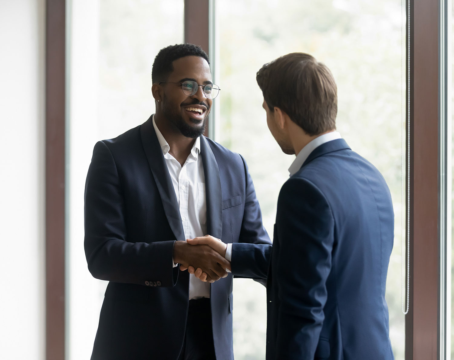 Two business professionals shaking hands and smiling, symbolizing successful relationship management and partnership in a modern corporate setting.