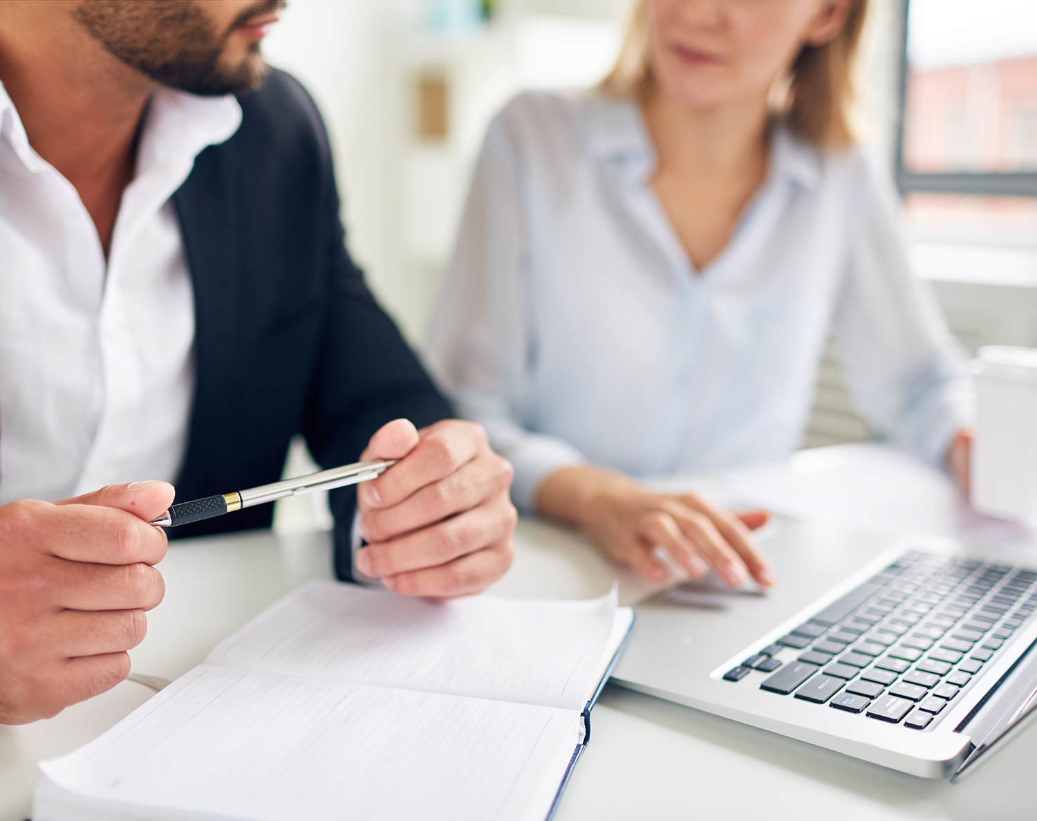 Two business professionals analyzing financial reports with charts and graphs, using sticky notes and a calculator for planning at a collaborative workspace.