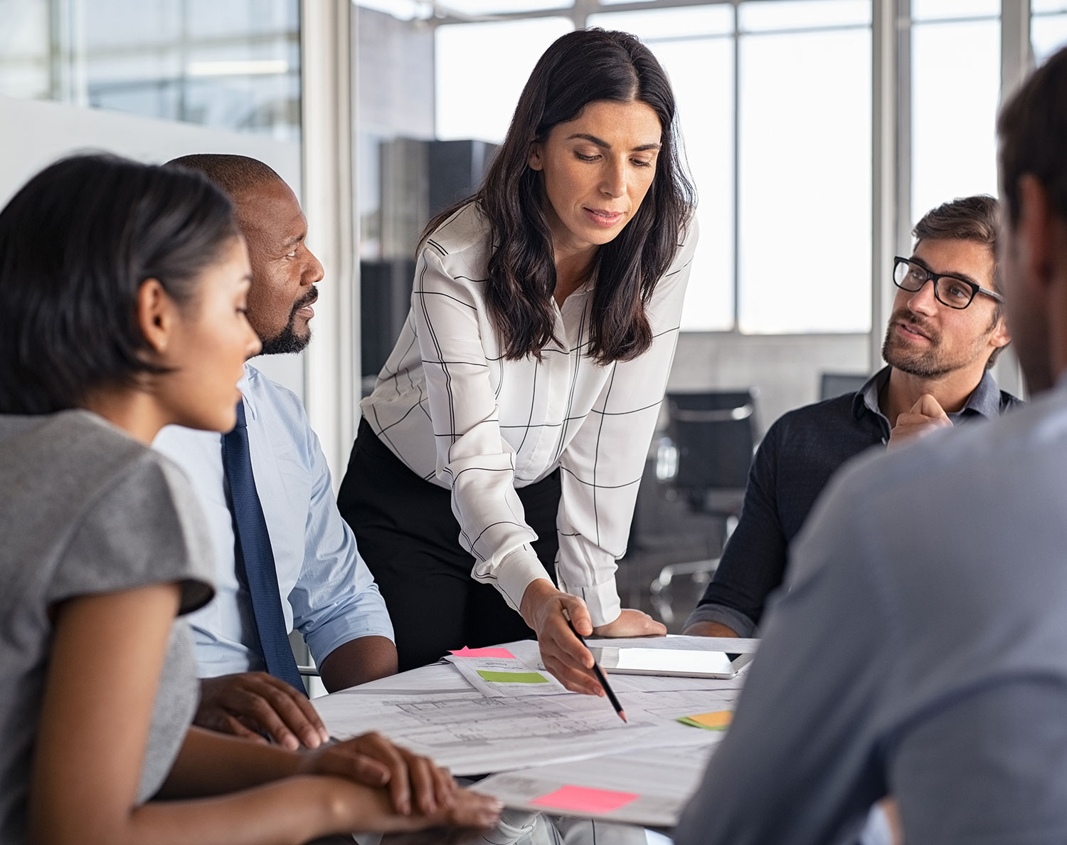 Confident leader guiding a business team in a strategic discussion, reviewing documents and sharing insights in a modern office setting.